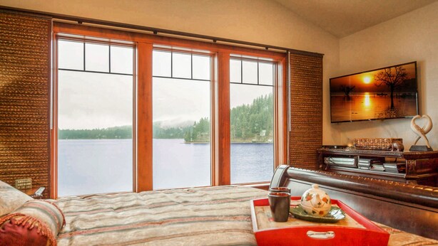 A hotel room with a large window offering a view of a lake and forest. There is a bed with a red tray and a teapot on it.