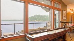 A room with large windows overlooking a lake, a billiards table, and a telescope.