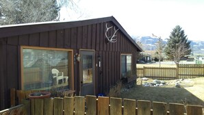 Een houten chalet met een omheinde tuin, een groot raam en een deur.