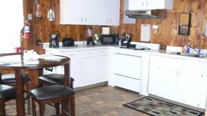 Een keuken met witte kasten, een fornuis, een magnetron en een koffiezetapparaat. Er staat een eettafel met stoelen en een vloerkleed met dierenprint.