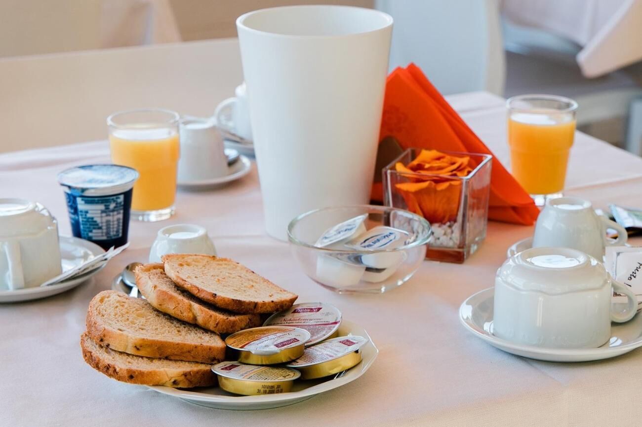 Una mesa de desayuno con pan, mantequilla, mermelada, leche y jugo de naranja.