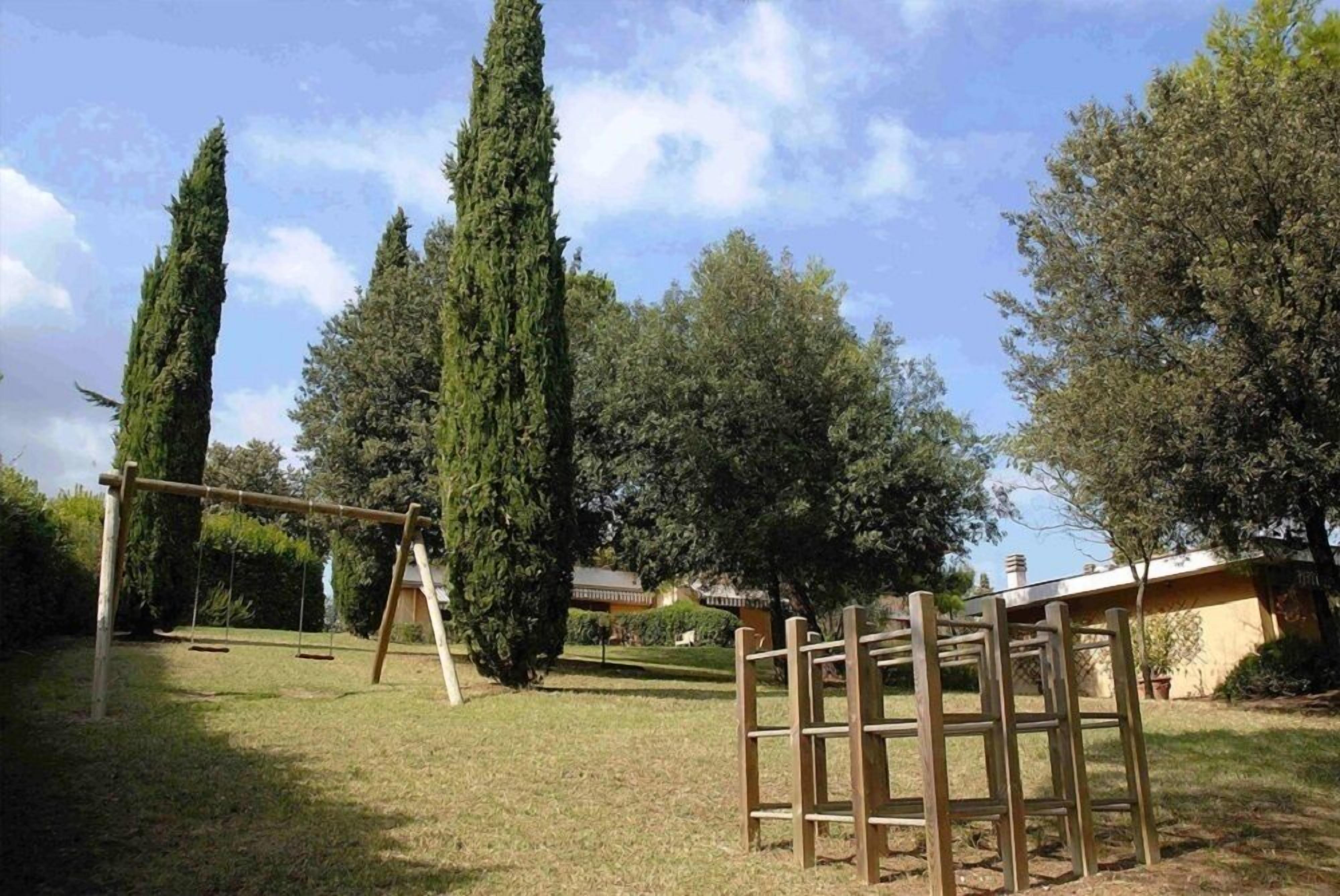 A backyard with a swing set, tall trees, and a wooden structure.