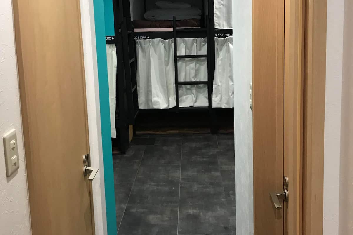 Um corredor estreito que leva a um quarto com beliche, parede de destaque em tom de verde-água e piso ladrilhado.