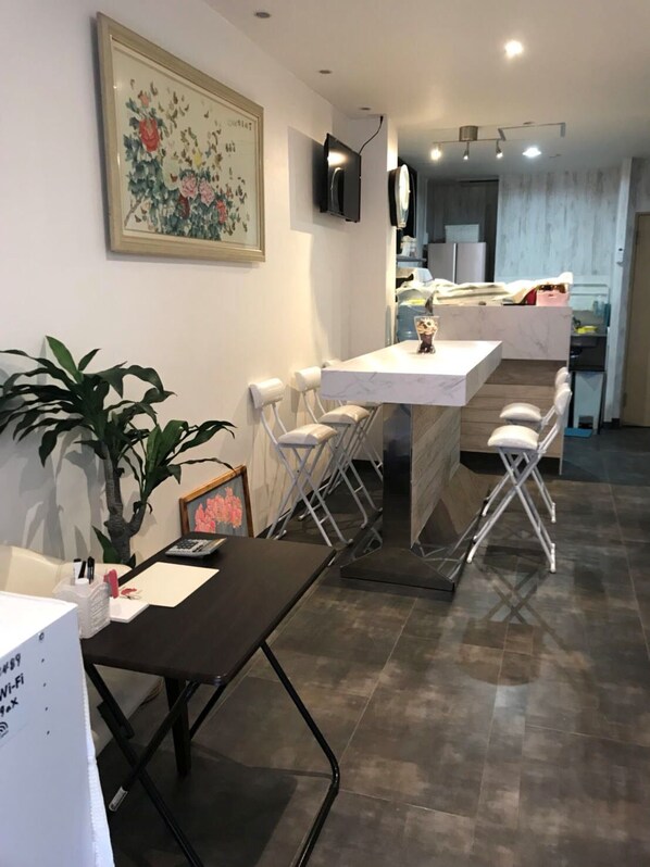 A modern kitchen with white countertops, a built-in oven, and a microwave. There is a dining area with a table and chairs, and a large potted plant.