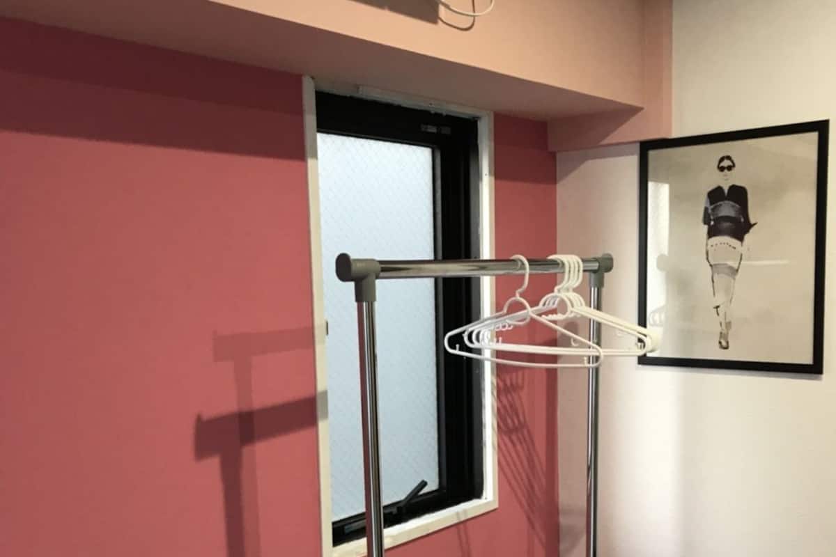 Quarto com janela, ar-condicionado fixado na parede, varal de roupas e uma obra de arte emoldurada.