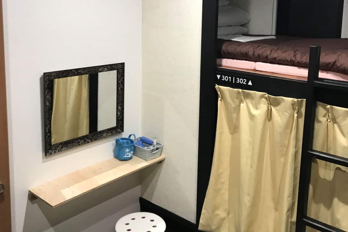 Quarto com beliche, uma pequena escrivaninha, espelho e prateleira com uma mala e uma caixa.