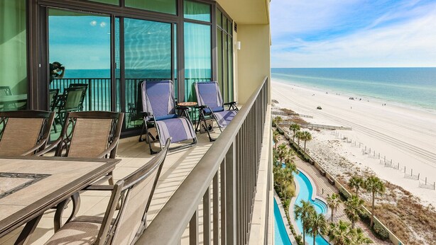 A balcony with chairs and a table, overlooking a beach and a pool. - Phoenix West ~ 8th FLOOR! ~ Condo 802 ~ 3BR 4 BA (Orange Beach)