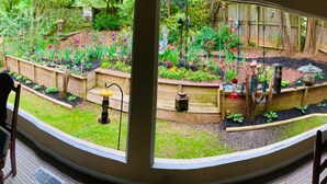 Un jardín con bancales elevados, un comedero para pájaros y una pequeña estatua.