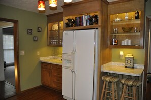 Une cuisine avec des meubles de rangement en bois, un réfrigérateur blanc et des tabourets de bar.