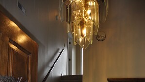 Una escalera con barandilla de madera, un candelabro y un espejo con marco decorativo.