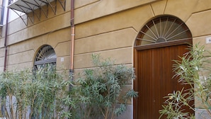 A building with a wooden door, a balcony, and planters with plants. - Appartamento moderno alla Cala by Wonderful Italy (Palermo)