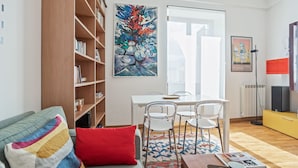 A modern living room with a sofa, a dining table with chairs, a bookshelf, and artwork on the walls. - Appartamento moderno alla Cala by Wonderful Italy (Palermo)
