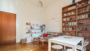 A living room with a wooden floor, a white sofa, a coffee table, a dining table with chairs, and a bookshelf filled with books. - Appartamento moderno alla Cala by Wonderful Italy (Palermo)