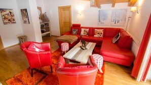 A cozy living room with a red sofa, matching armchairs, and a coffee table. - Penthouse All Seasons Lodge (Kaprun)