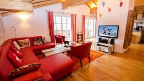 A cozy living room with a red sofa, a television, and wooden beams on the ceiling. - Penthouse All Seasons Lodge (Kaprun)