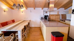 A cozy kitchen with wooden beams, a dining table with chairs, and a built-in island with a sink. - Penthouse All Seasons Lodge (Kaprun)