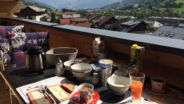 A balcony with a table set for breakfast, including a coffee cup, a glass of juice, and a plate with a sandwich. - Penthouse All Seasons Lodge (Kaprun)