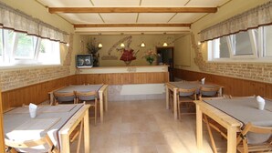 A rustic interior with wooden tables and benches, a brick wall, and a reception area with a counter and decorative elements.