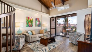 A spacious living area with a wooden staircase, a sofa set, a coffee table, and a view of the outdoors through a glass door. - Kamaole Sands 3-406 - Modern Kitchen, Large Lanai, Enclosed Private MB, Split AC (Kihei)