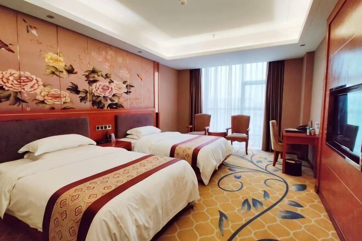 Een hotelkamer met twee bedden, een bureau, een televisie en een groot raam.