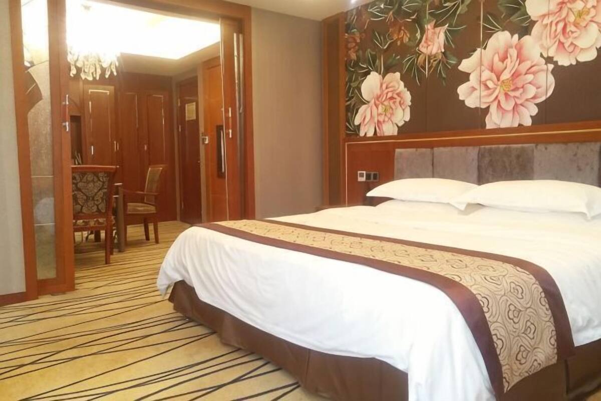 Een hotelkamer met een groot bed, een houten garderobe, een bureau met stoel, en een bloemen behang.