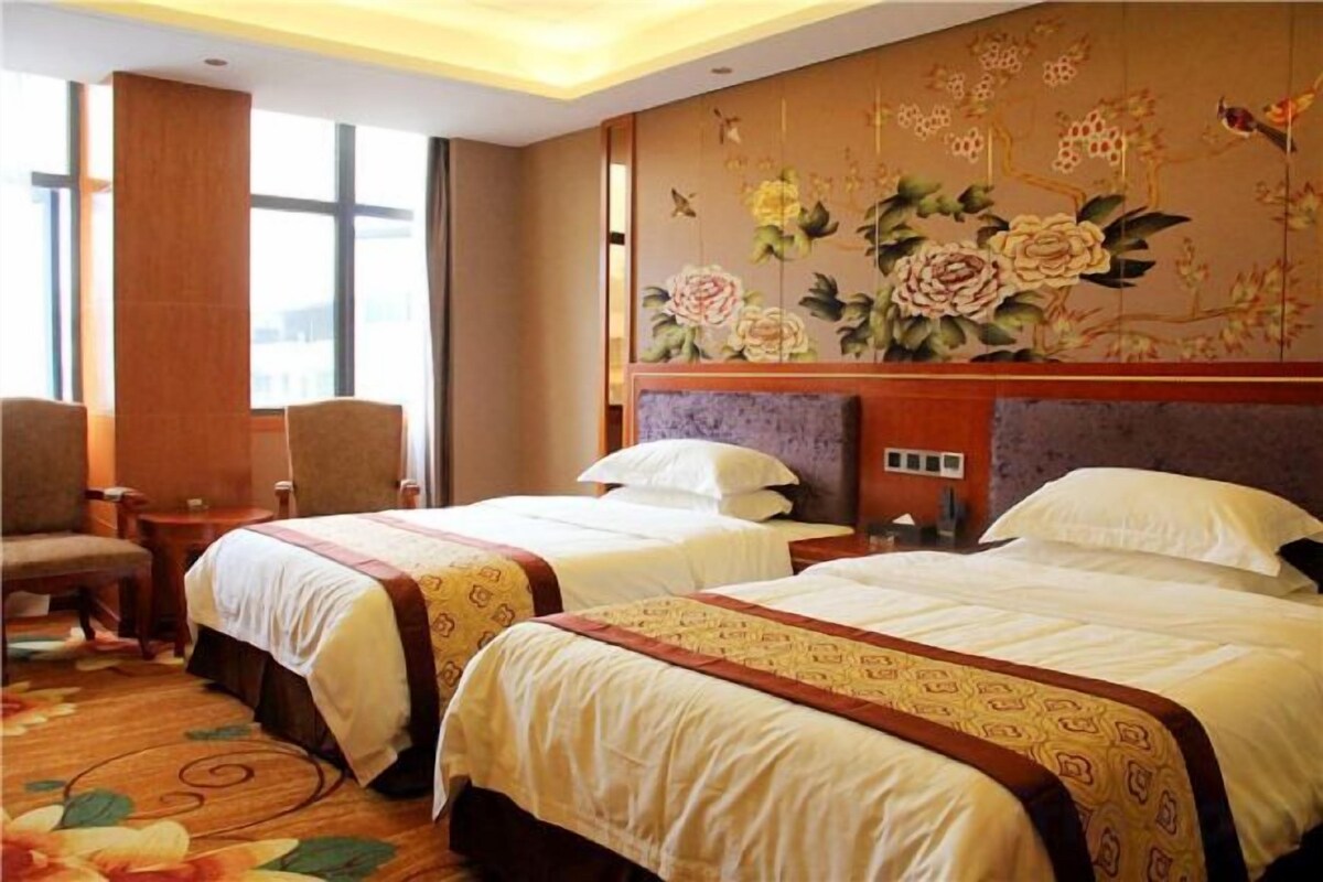 A hotel room with two beds, a large window, and a floral wall mural.