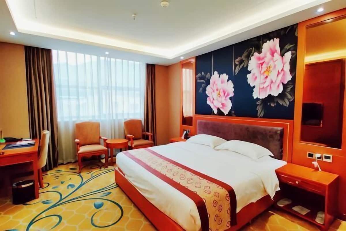 Een hotelkamer met een groot bed, een bureau, een stoel en een groot raam.