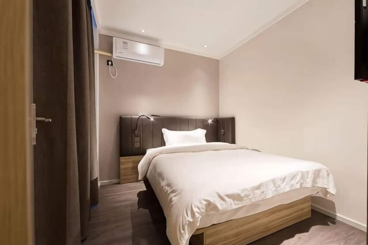 A bedroom with a bed, a headboard, a wall-mounted air conditioner, and a door.