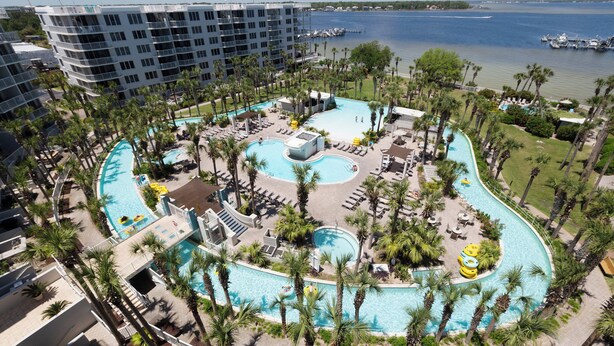 Een resort met een groot centraal zwembad, meerdere kleinere zwembaden en een jachthaven op de achtergrond.