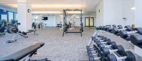 Un gimnasio con varios equipos de ejercicio, incluyendo cintas de correr, máquinas de pesas y mancuernas.