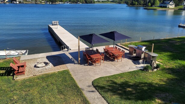 Een terras aan het meer, met tuinmeubilair en een barbecue, met uitzicht op een rustig meer.