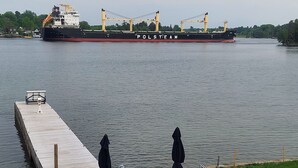 Een steiger met zitplaatsen buiten en een groot vrachtschip op de achtergrond.