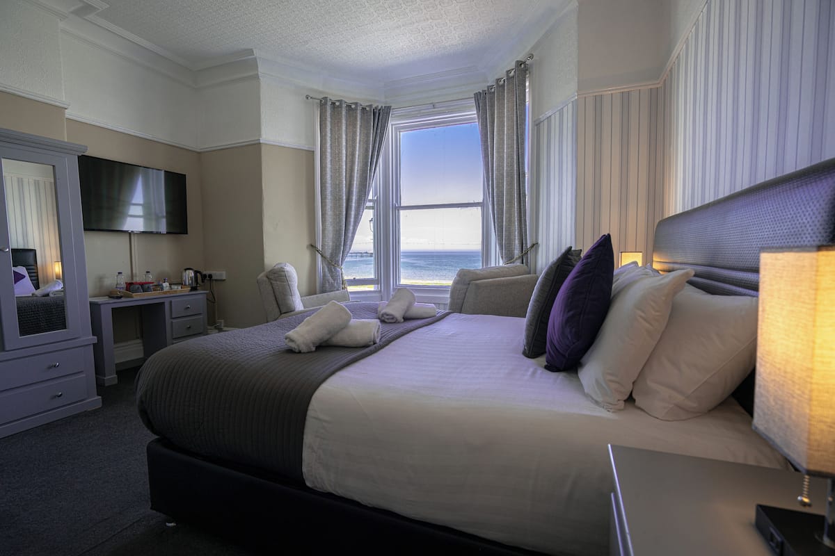A hotel room with a large bed, a desk, a TV, and a view of the ocean.