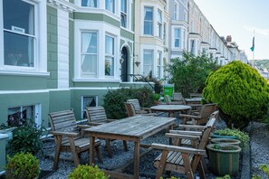 A row of Victorian-style townhouses with bay windows, outdoor seating with wooden tables and chairs, and a well-maintained garden with potted plants. - The Central Hotel (Llandudno)