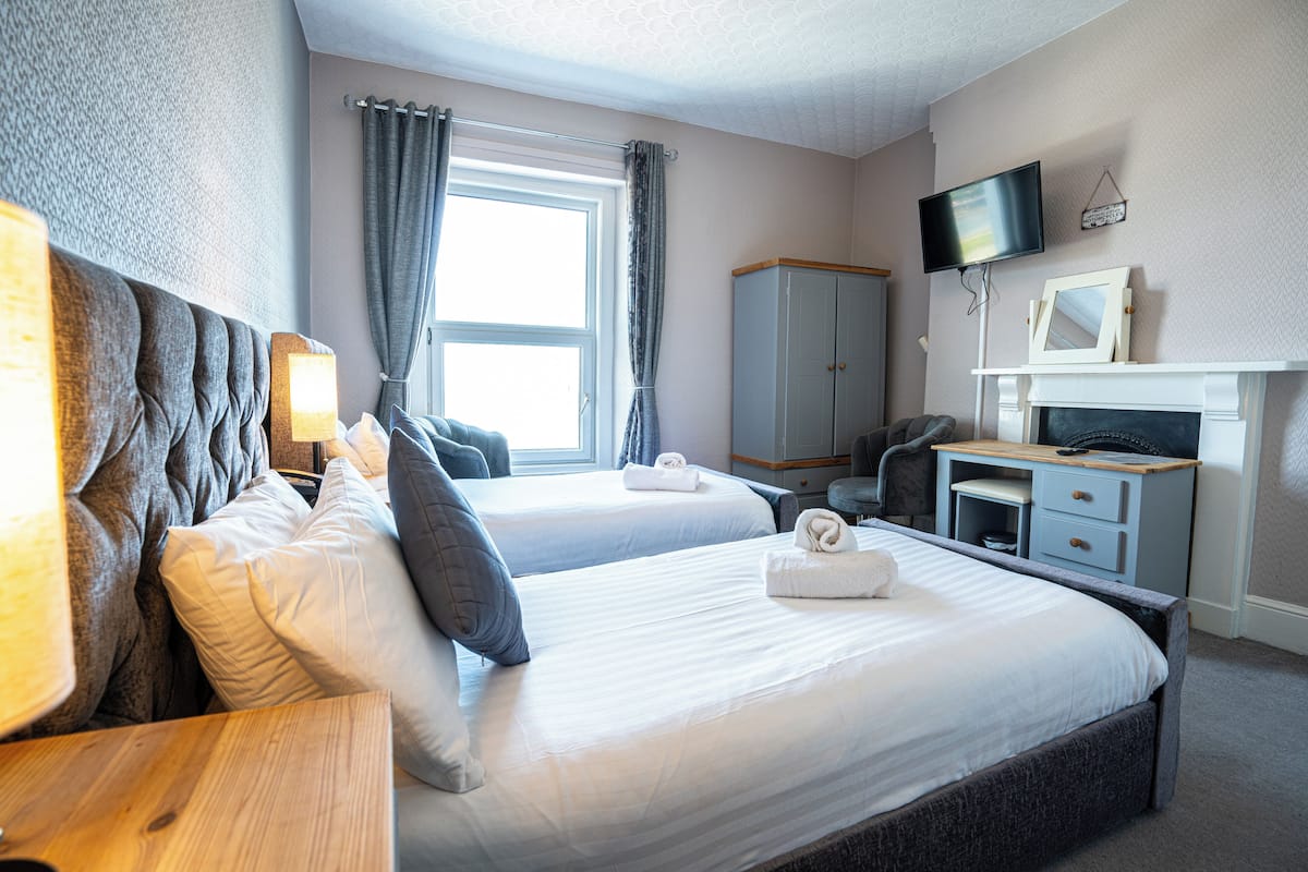 A hotel room with two beds, a desk, a television, and a fireplace.