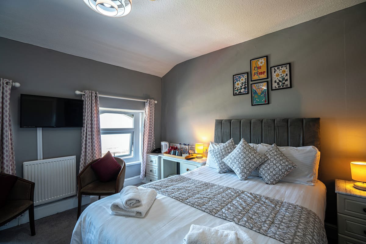 A neatly arranged bedroom with a bed, bedside tables, a chair, a desk, and a television.