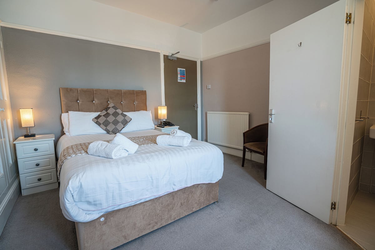 A neatly made bed with white linens, a bedside table with a lamp, and a chair in a hotel room.