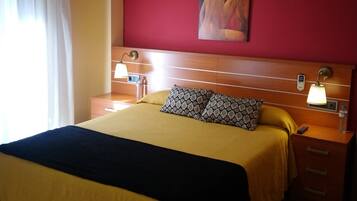 Hotellihuone, jossa on sänky, yöpöytä, lamppu, taulu ja ikkuna, jossa on verhot.