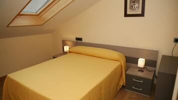 A bedroom with a skylight, a bed with a yellow bedspread, bedside lamps, a nightstand, and a framed picture on the wall.