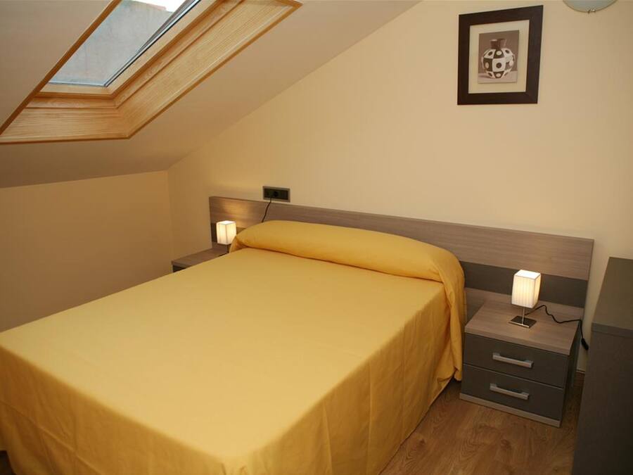 A bedroom with a skylight, a bed with a yellow bedspread, bedside lamps, a nightstand, and a framed picture on the wall.