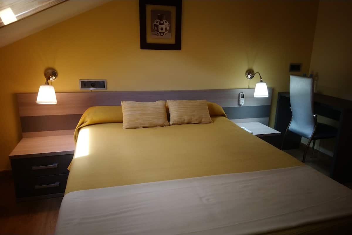 A hotel room with a bed, bedside tables, lamps, a desk, and a chair.