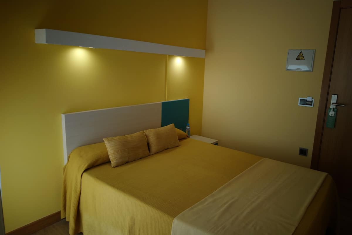 A hotel room with a bed, a nightstand, and a door.