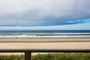 A beach with a person walking on the sand, a clear sky, and the ocean in the background.