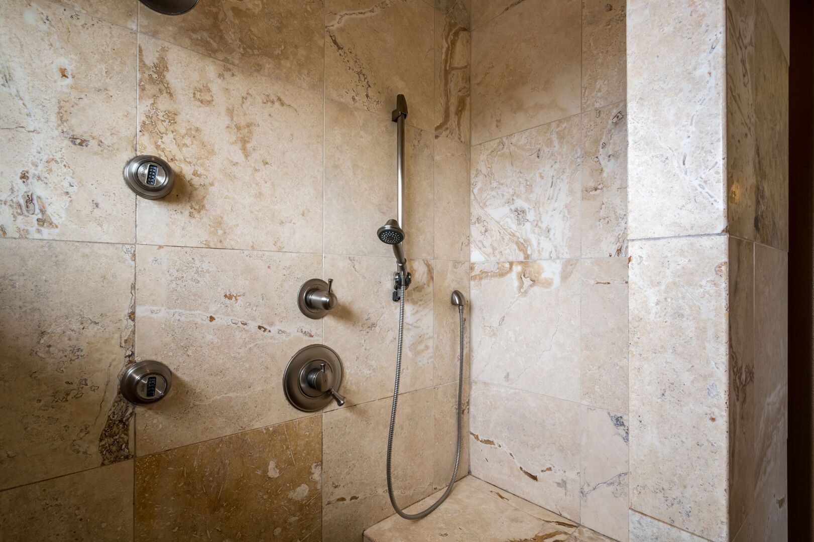 A shower with a handheld showerhead and a fixed wall-mounted faucet.