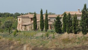 A stone building with a tiled roof, surrounded by trees and a fenced area.