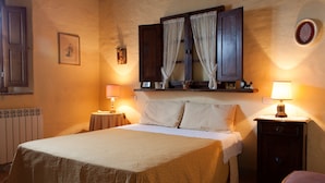 A neatly made bed with a white bedspread, two bedside lamps, a nightstand, and a window with curtains.