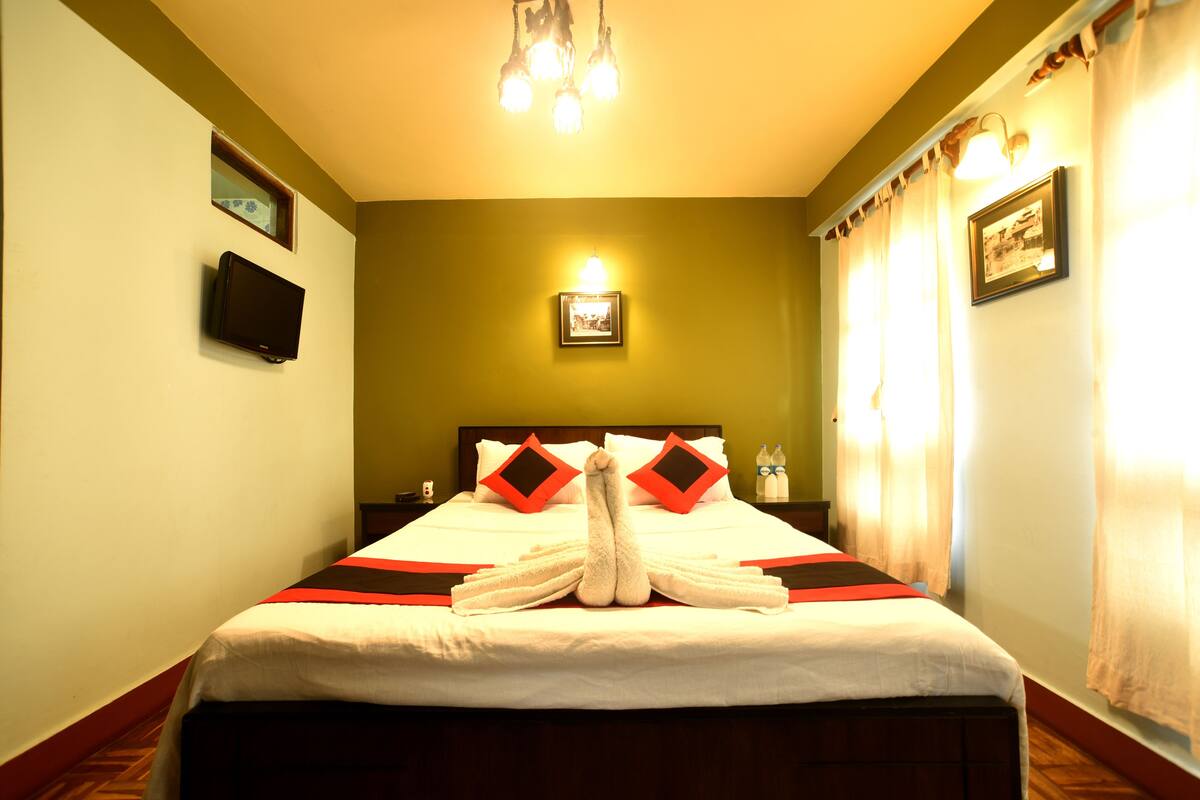 A hotel room with a neatly made bed, a television on the wall, and a framed picture above the bed.