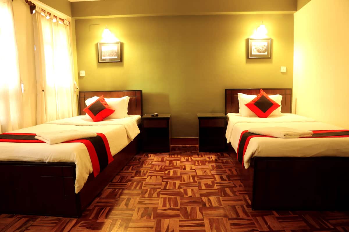 A hotel room with two beds, wooden parquet flooring, and wall-mounted lights.