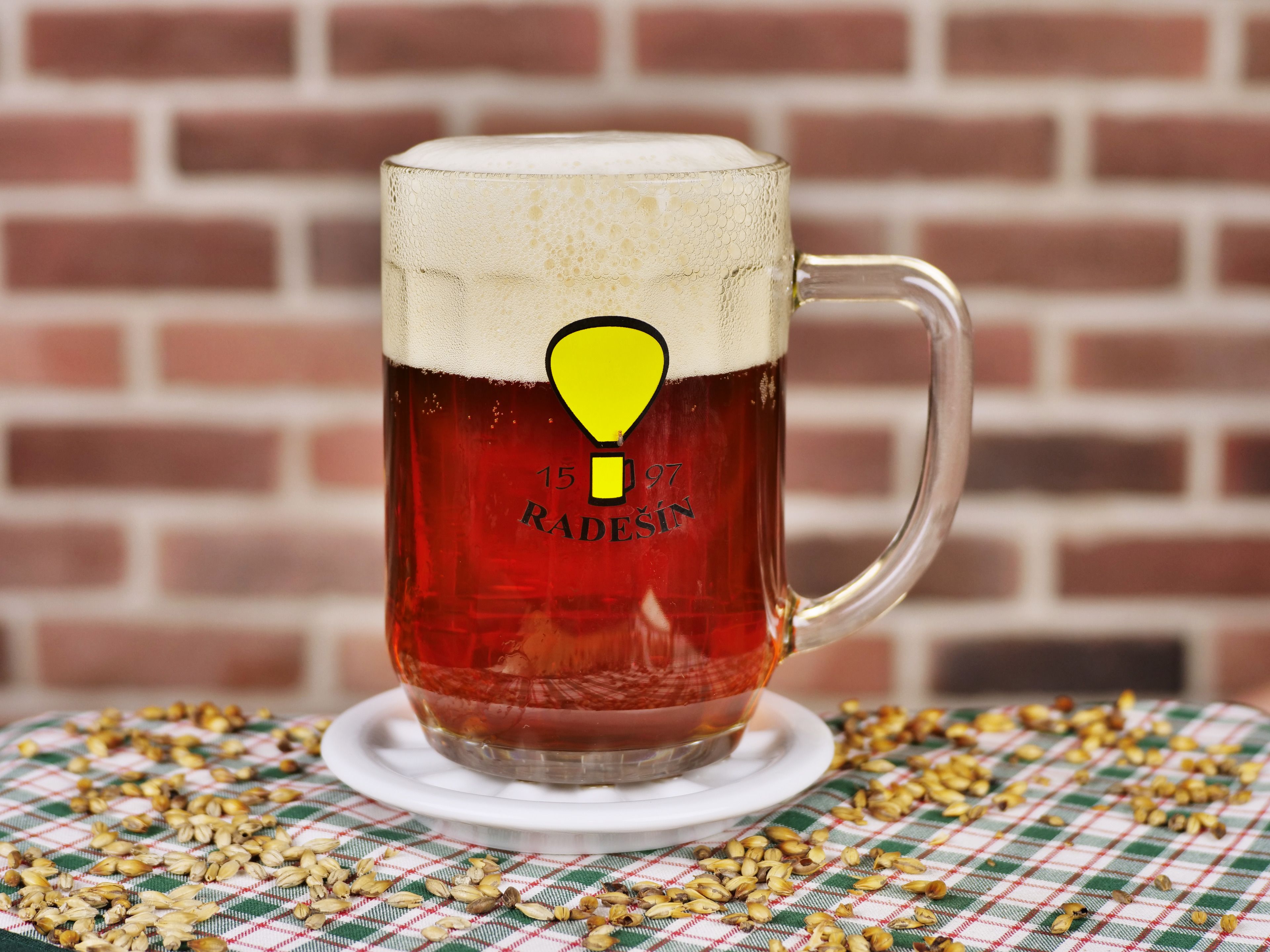 Une tasse en verre ornée d’un symbole représentant une ampoule jaune et du texte « RADESIN », le tout posé sur une nappe à carreaux.