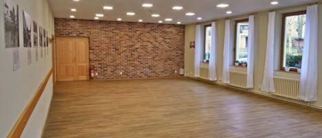 A spacious room with a wooden floor, brick wall, and large windows with white curtains.